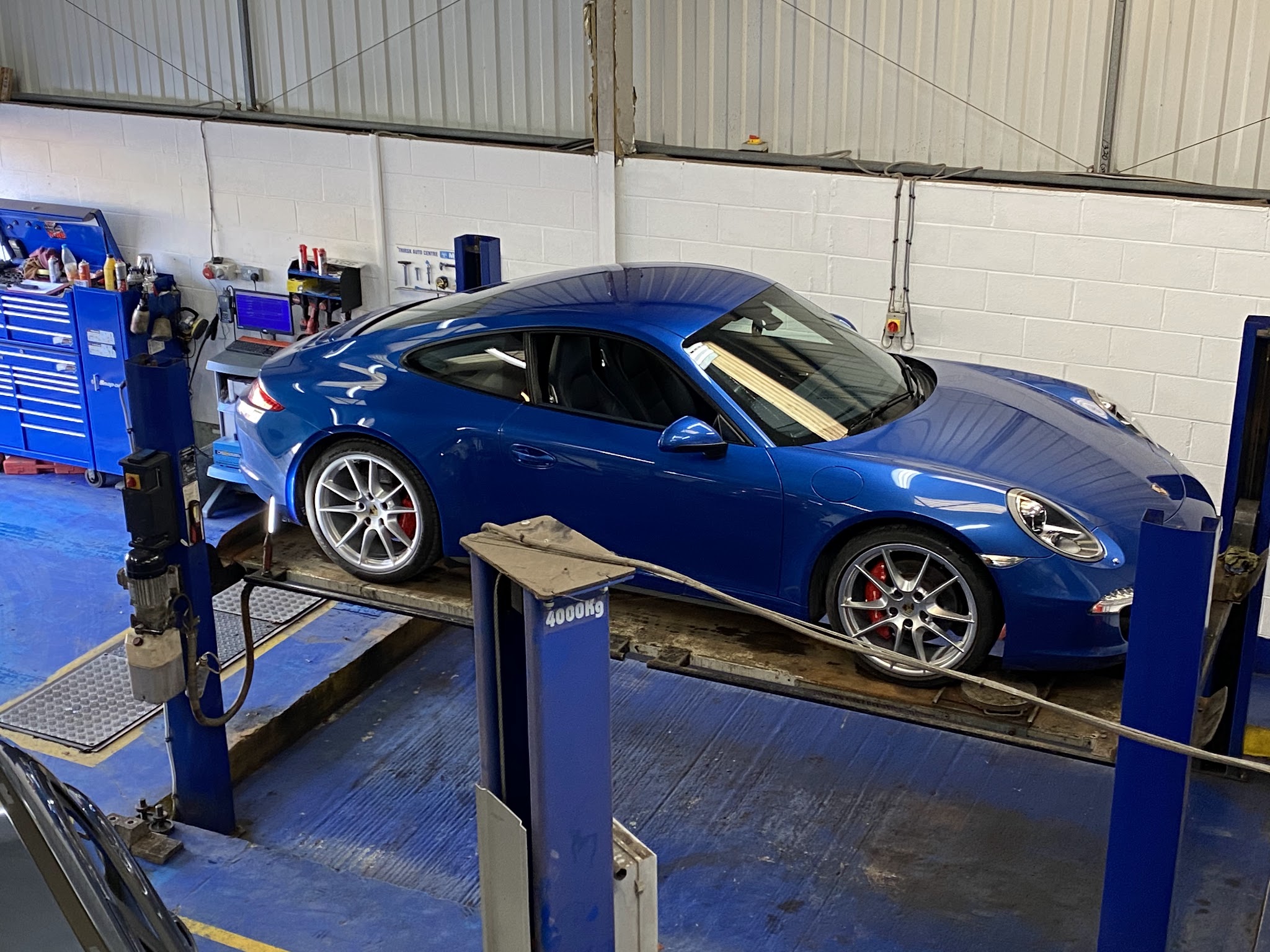 Blue Porsche 911 raised on a two-post lift in the Thirsk Autocentre workshop